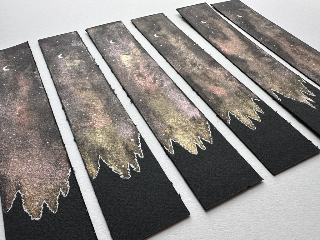 “The Whole Sky” handpainted bookmarks features a bright night sky beyond the silhouette of a forest.